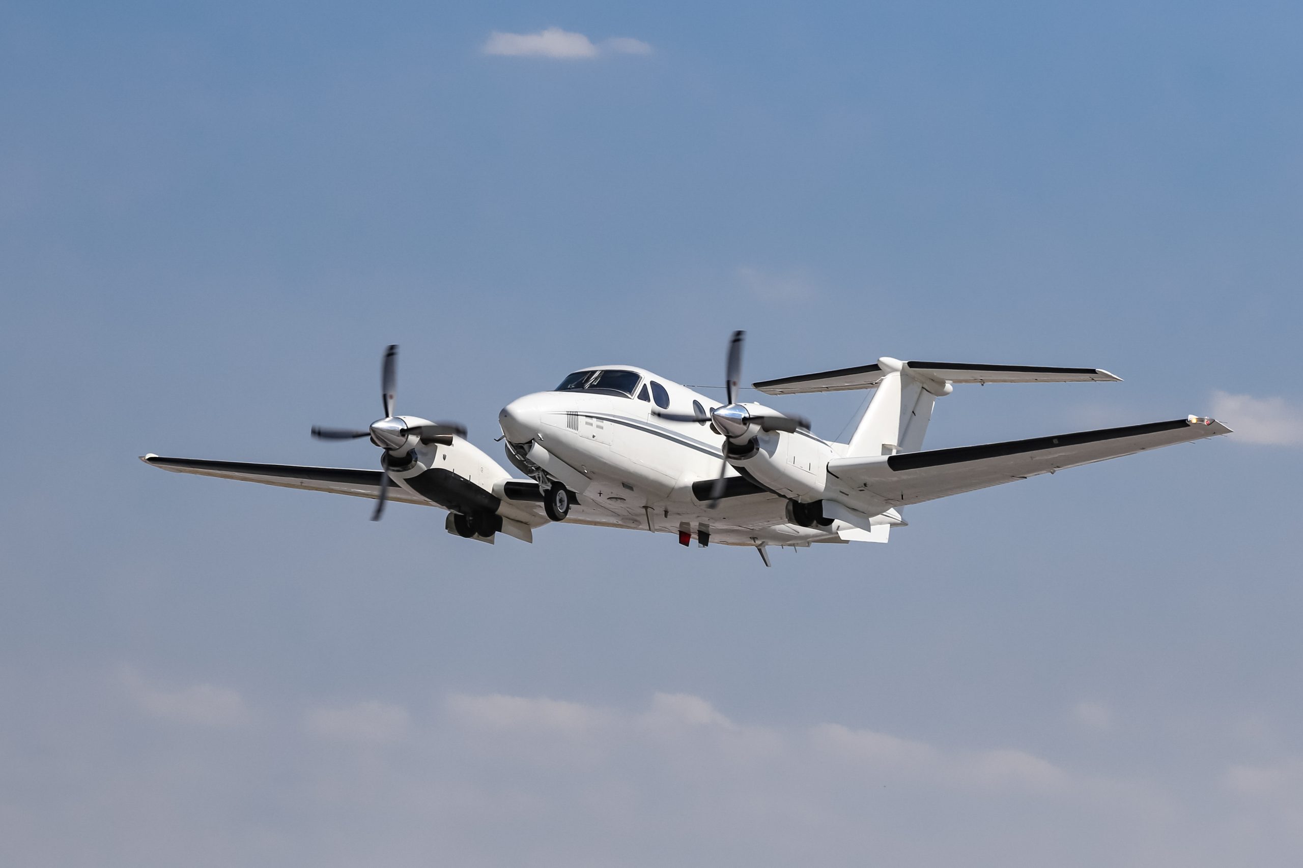 A white turboprop aircraft with two engines in flight against a clear blue sky